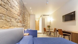 A modern hotel room with a stone wall, a sofa, a desk, and a TV. - Le stanze degli amidei (Florence)