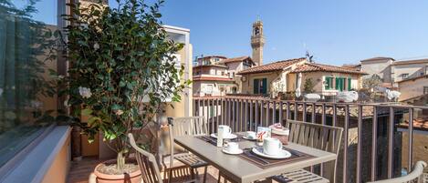 A balcony with a table set for two, potted plants, and a view of the town.