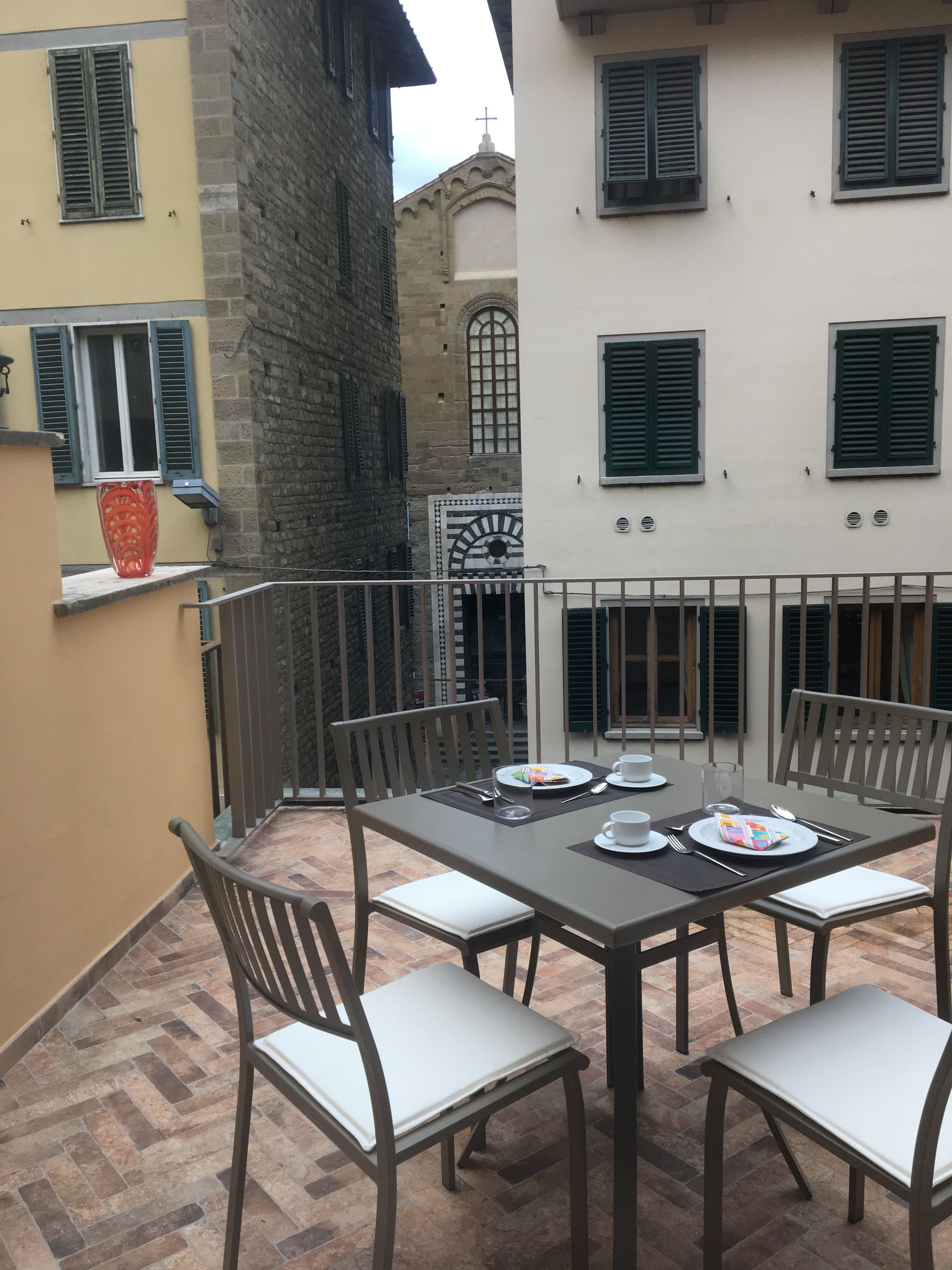 An outdoor dining area with a table set for four, surrounded by chairs, on a tiled patio.