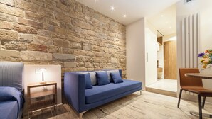 A modern living room with a stone wall, a blue sofa, a wooden side table with a lamp, and a dining area with a chair and table. - Le stanze degli amidei (Florence)