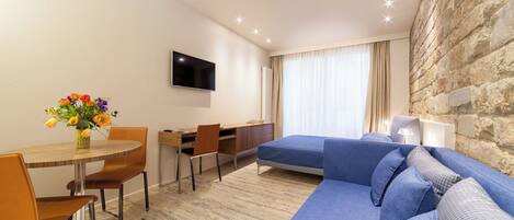 A modern hotel room with a dining area, a flat-screen TV, a sofa, and a stone accent wall.