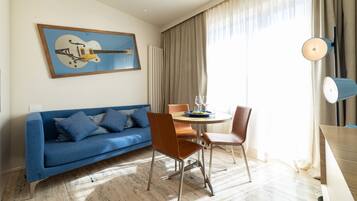 En moderne stue med en blå sofa, et spisebord med stole, et guitarbillede på væggen og en lampe.