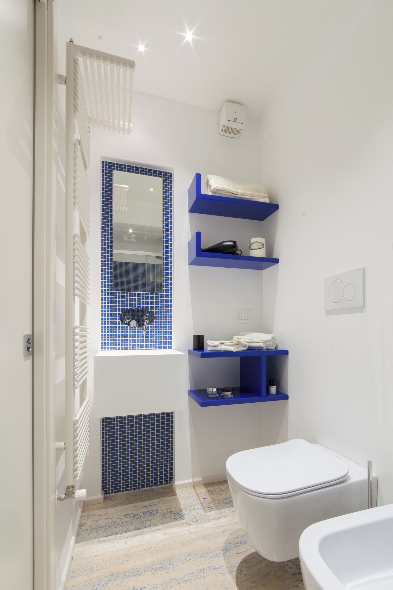 Un baño con inodoro blanco, zona de ducha con azulejos azules y lavamanos blanco.