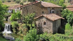 A stone building with a tiled roof, surrounded by greenery and a small waterfall.