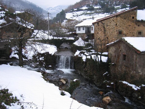 A stone building with a stone wall and a small waterfall. - La Casa de las Arcas (Vega de Liebana)