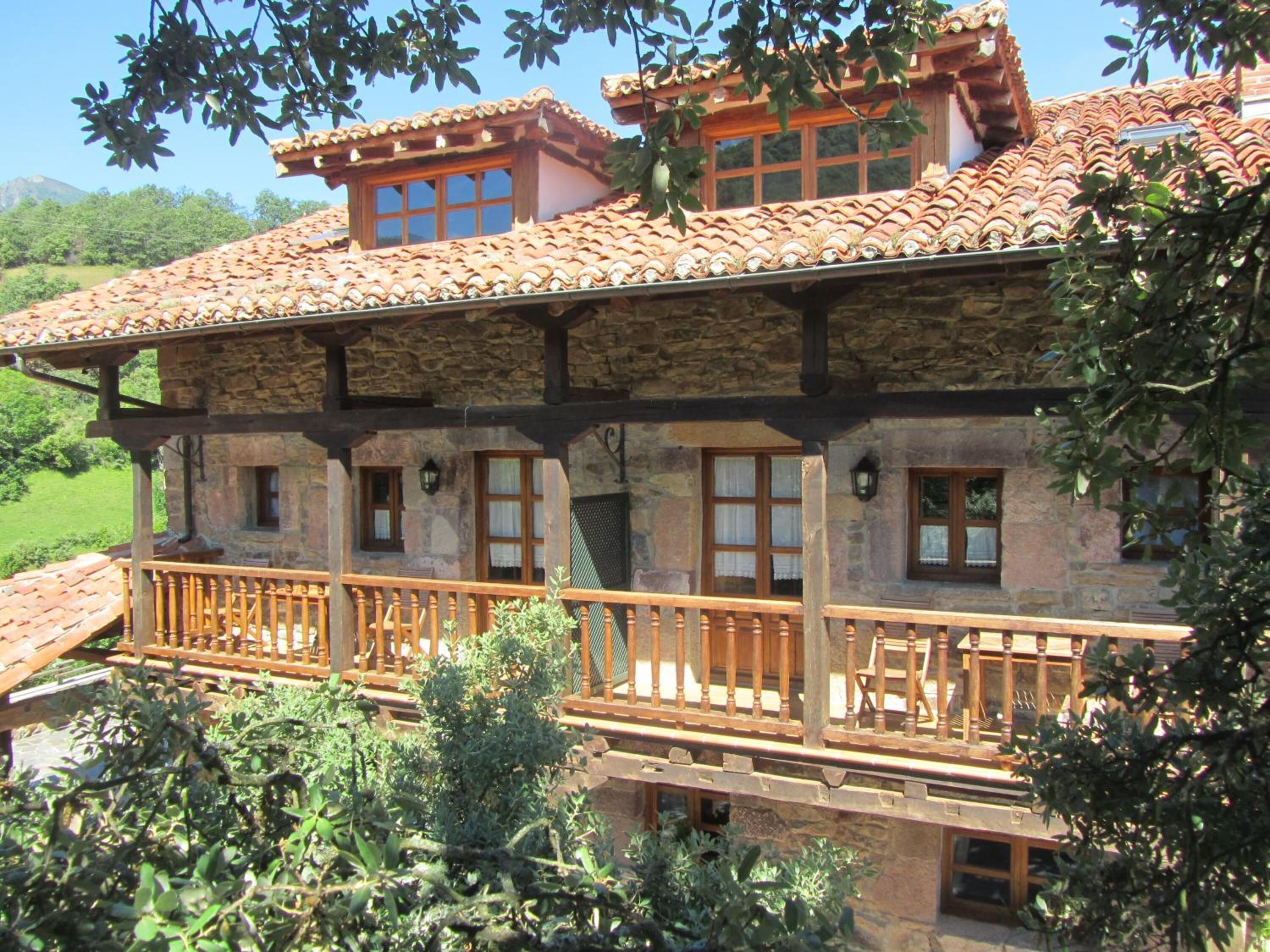 A stone building with a tiled roof, wooden balcony railings, and multiple windows.
