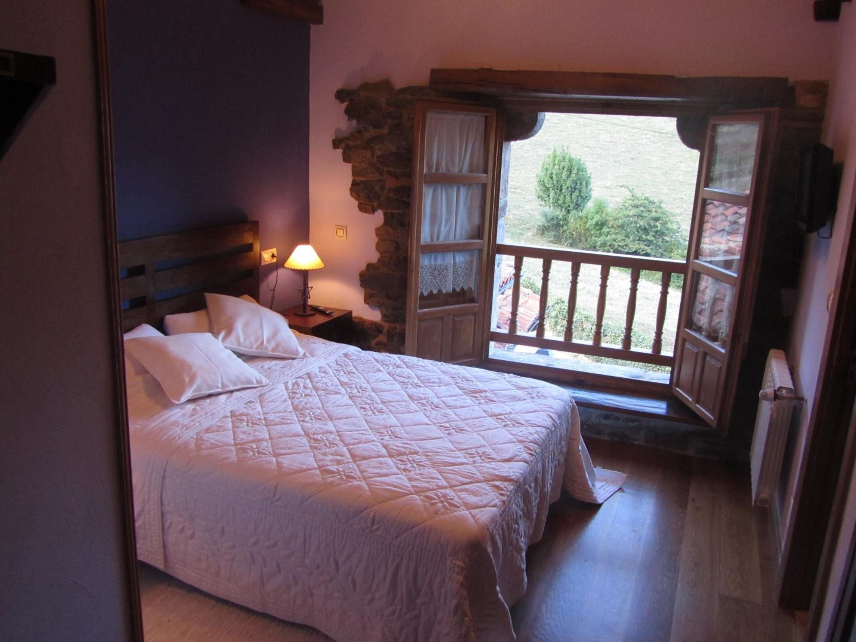 A bedroom with a bed, a nightstand, a lamp, and a window with a view of greenery.