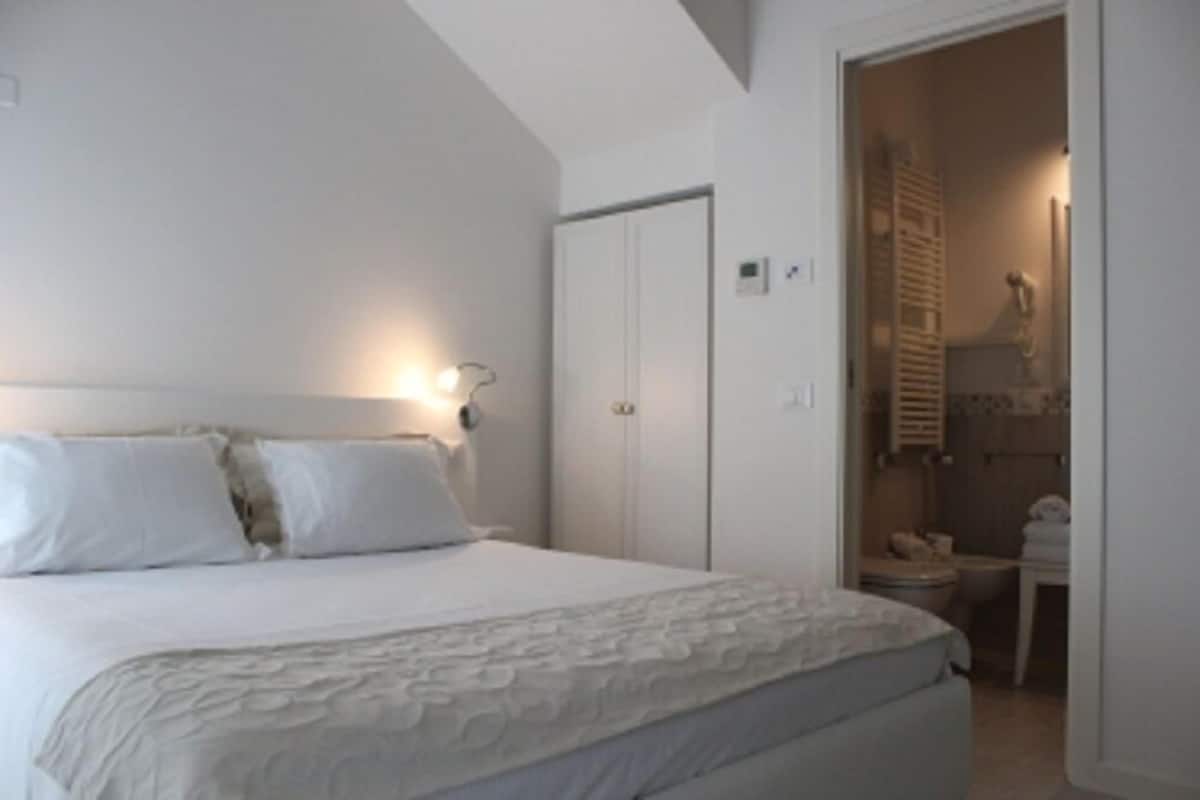 A bedroom with a large bed, a wardrobe, and a bathroom visible through an open door.