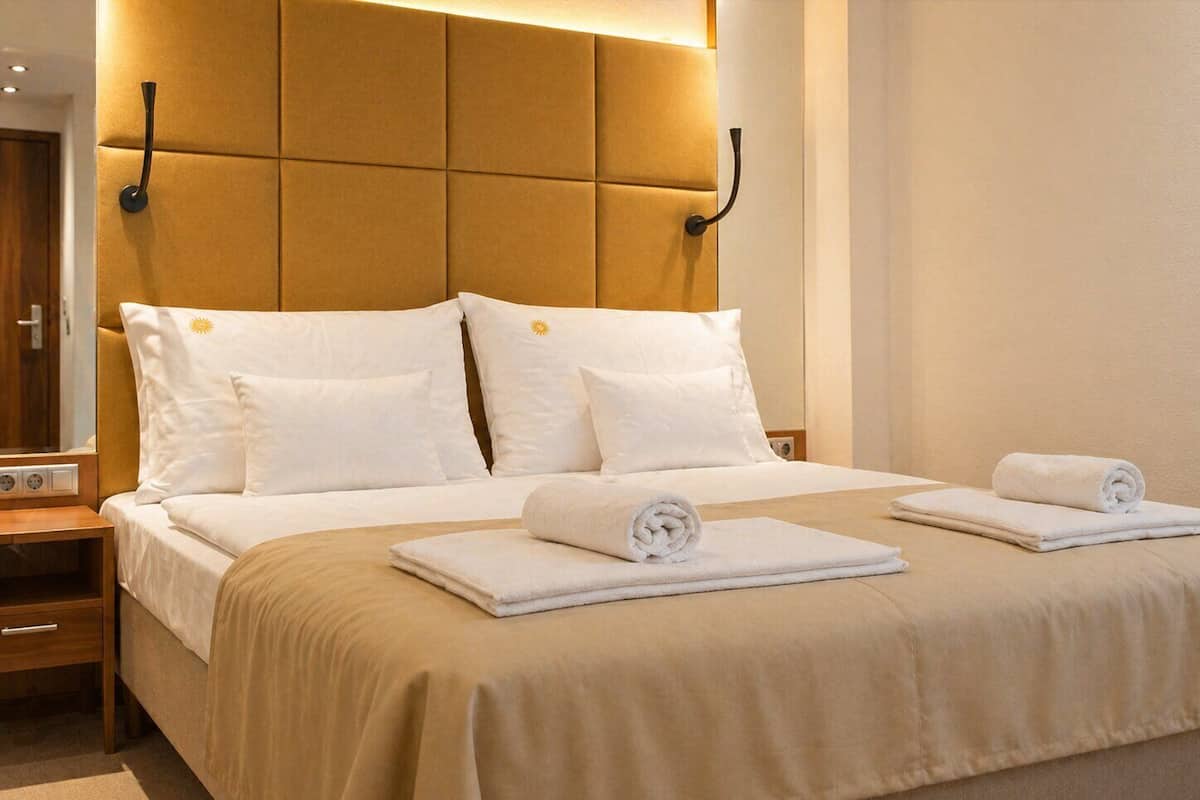 Une chambre d’hôtel avec un grand lit, deux tables de chevet, une petite table et une tête de lit dotée d’un éclairage intégré.