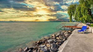 A lakeside view with a pier, a tree, and a clear sky. - Világos Hotel Balatonvilágos (Balatonvilagos)