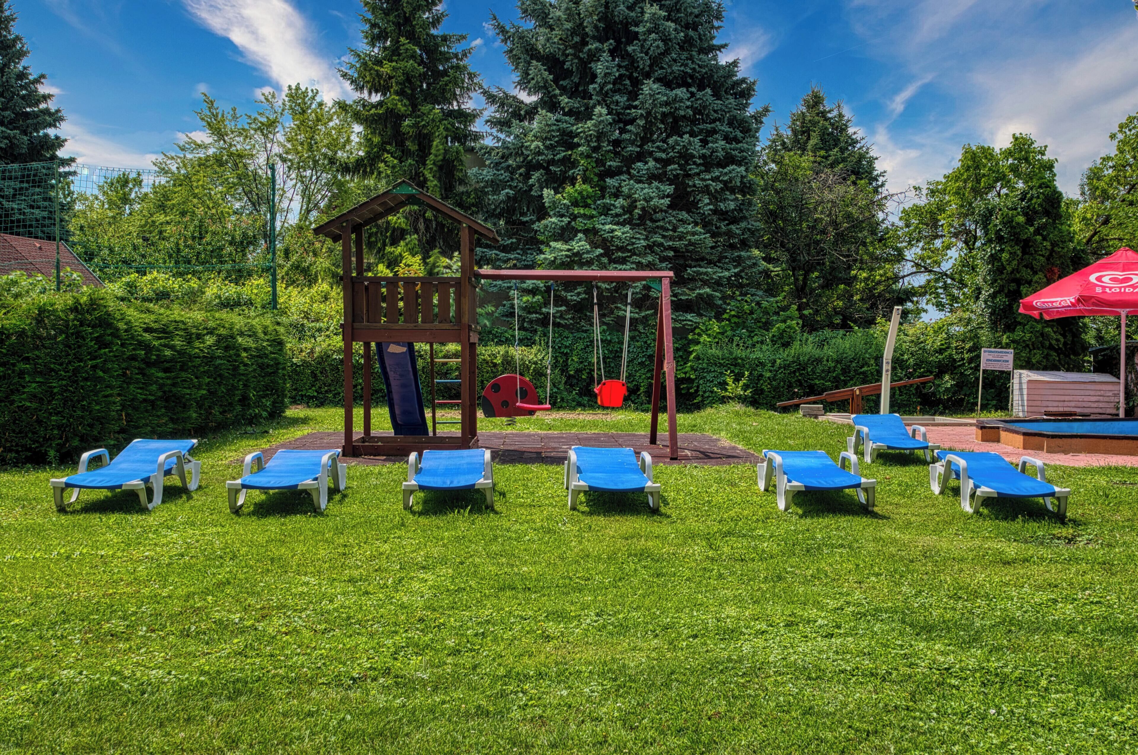 Une aire de jeux avec des balançoires, un toboggan et une petite structure en bois. On y trouve six fauteuils bleus disposés en rangée.