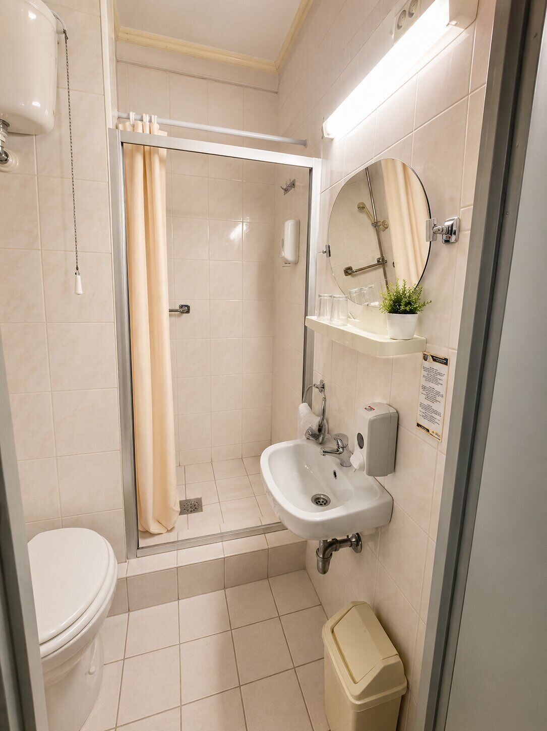 Un baño moderno con ducha, inodoro, lavamanos y un pequeño cubo de basura.