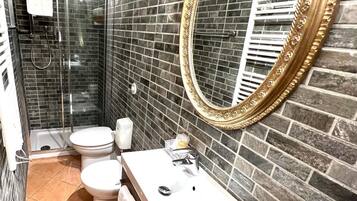 Ein Badezimmer mit Duschkabine aus Glas, einer weißen Toilette, einem Waschbecken inklusive Spiegel und einer gefliesten Wand.