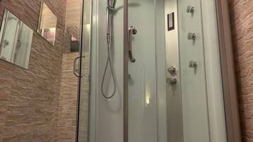 Una ducha a ras de suelo con mampara de vidrio, cabezal de ducha manual y panel de control en la pared.