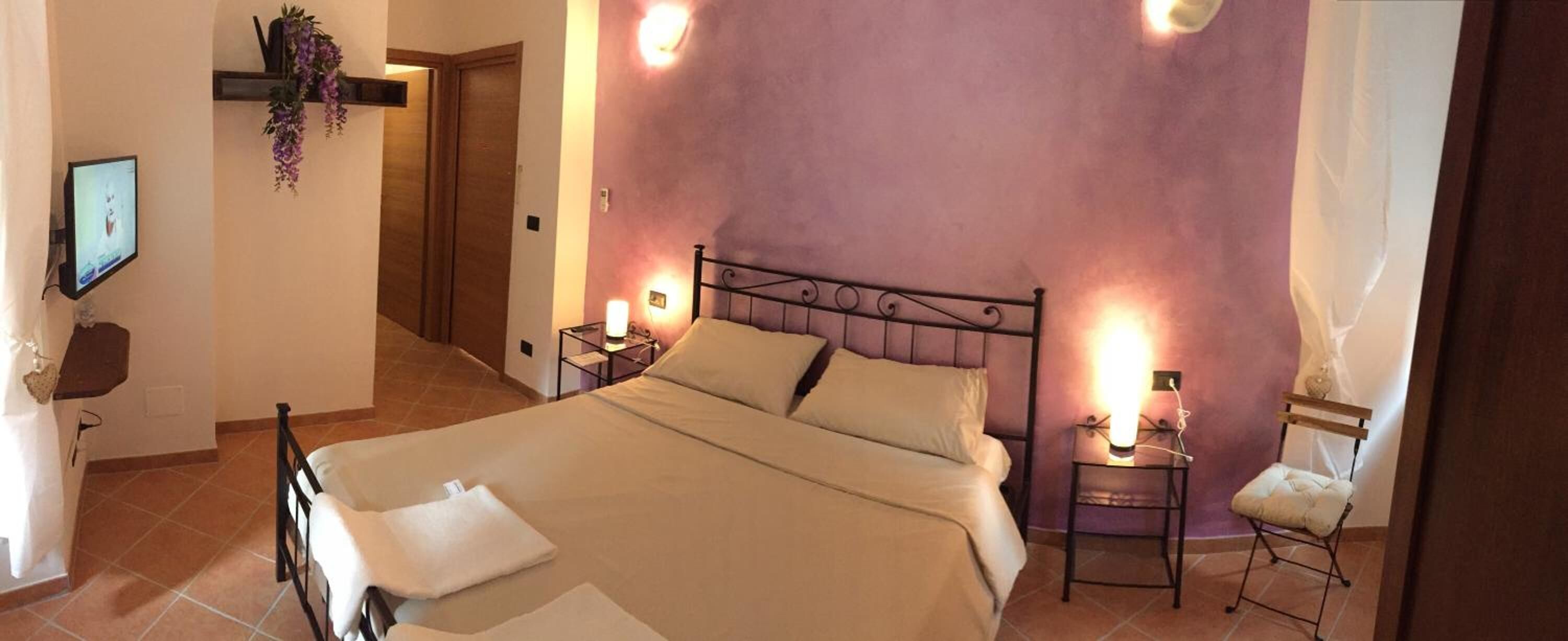 A bedroom with a bed, two bedside tables, a chair, a TV, and a door.
