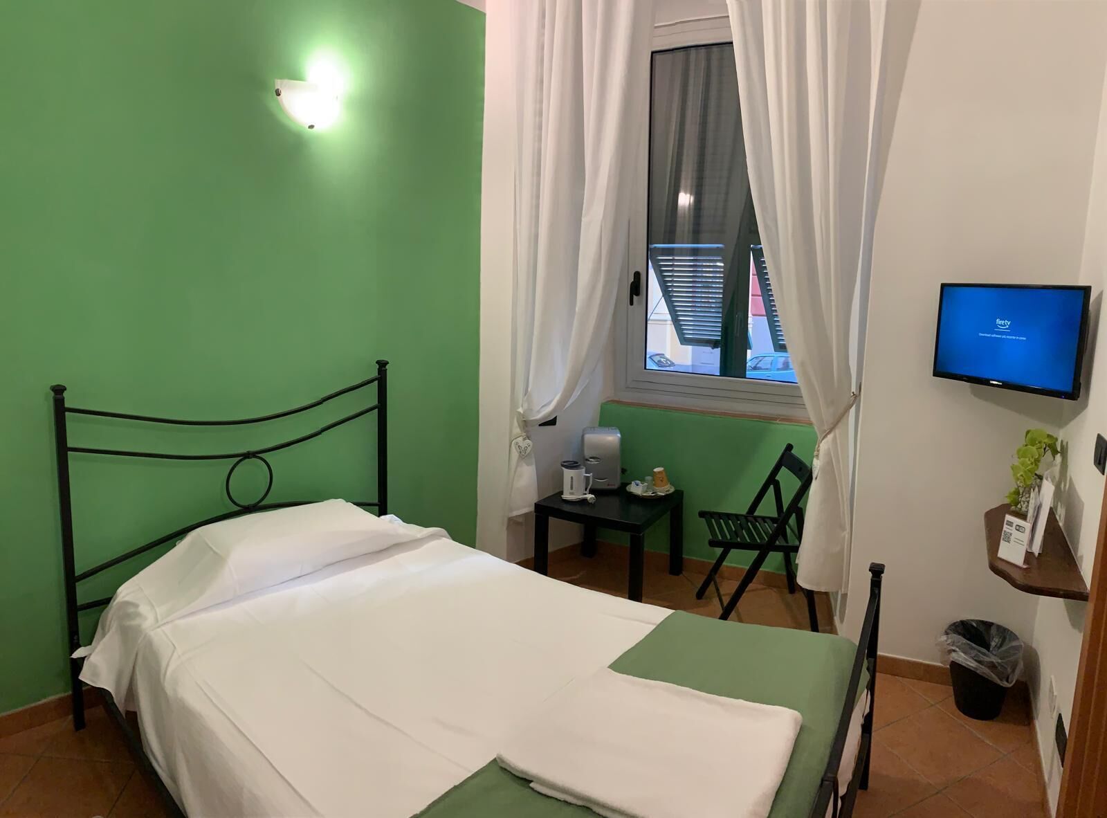 A small, clean room with a bed, a desk, a chair, a TV, and a window with curtains.