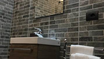 Ein Badezimmer mit modernem Design, das eine dunkle Ziegelwand, ein Waschbecken mit Spiegel darüber und zwei Handtücher an einem Handtuchhalter zeigt.