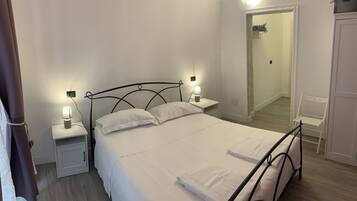 Un lit bien fait, avec du linge de lit blanc et des oreillers, deux tables de chevet avec des lampes, une armoire blanche et un miroir au mur.