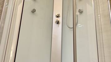 A glass-enclosed shower stall with multiple shower heads and a control panel.