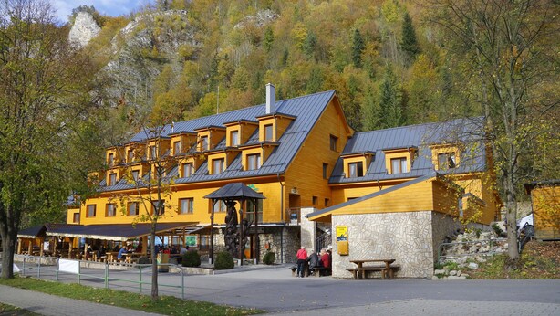 A multi-story hotel with a stone facade and a wooden upper structure, featuring outdoor seating and a mountain backdrop. - Chata Pieniny (Lesnica)