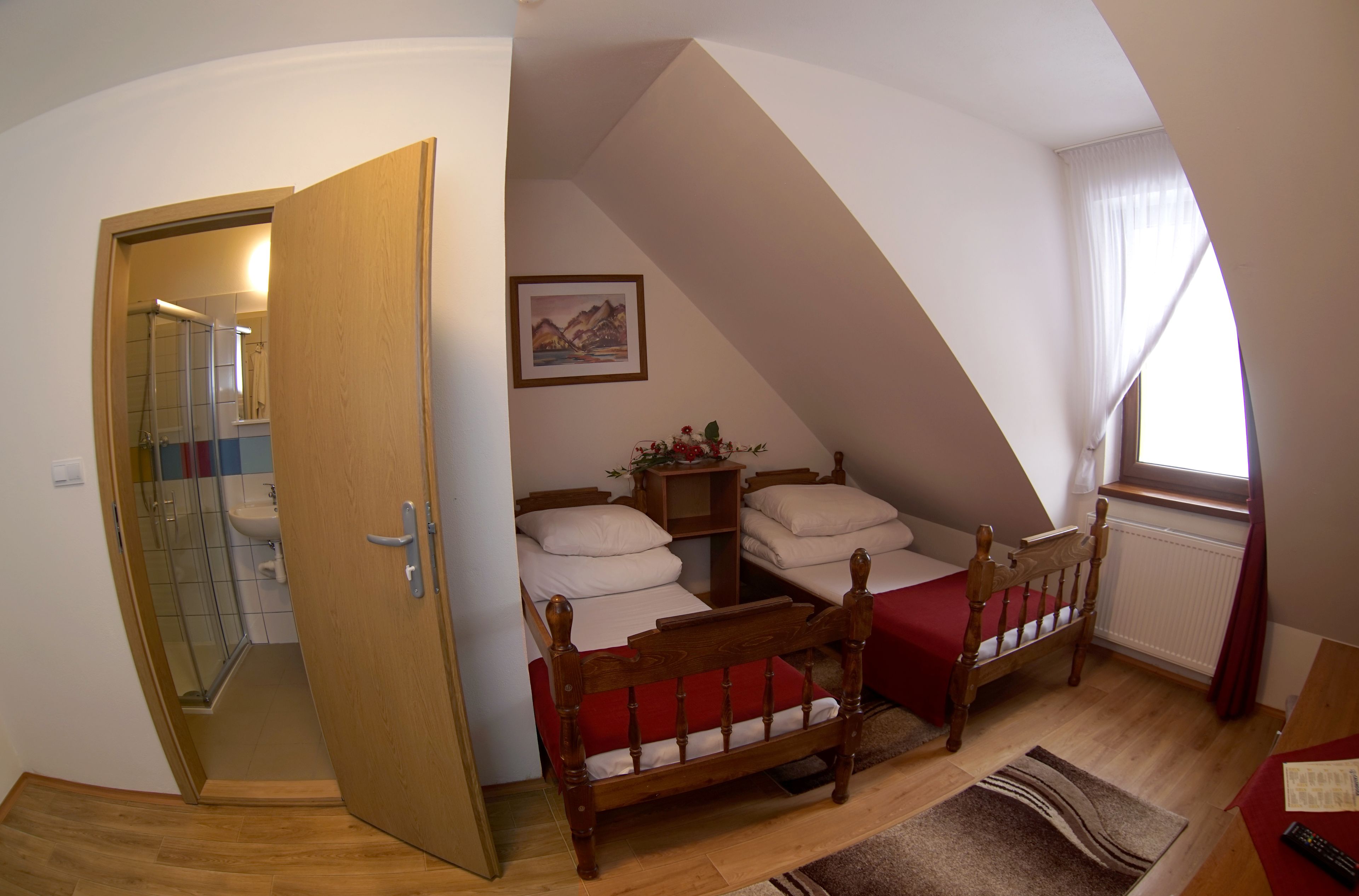 Camera da letto con due letti in legno, un comodino con una pianta, un quadro appeso al muro e una finestra con tende.