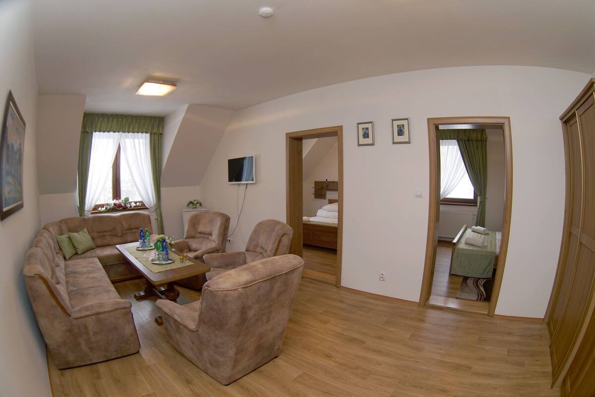 A spacious living area with a sofa set, a coffee table, and a television. There are wooden doors leading to other rooms.