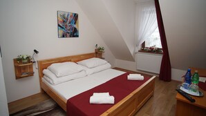 A bedroom with a wooden bed, white linens, a red bedspread, a painting on the wall, a window with curtains, and a bedside table with a remote control and bottles. - Chata Pieniny (Lesnica)