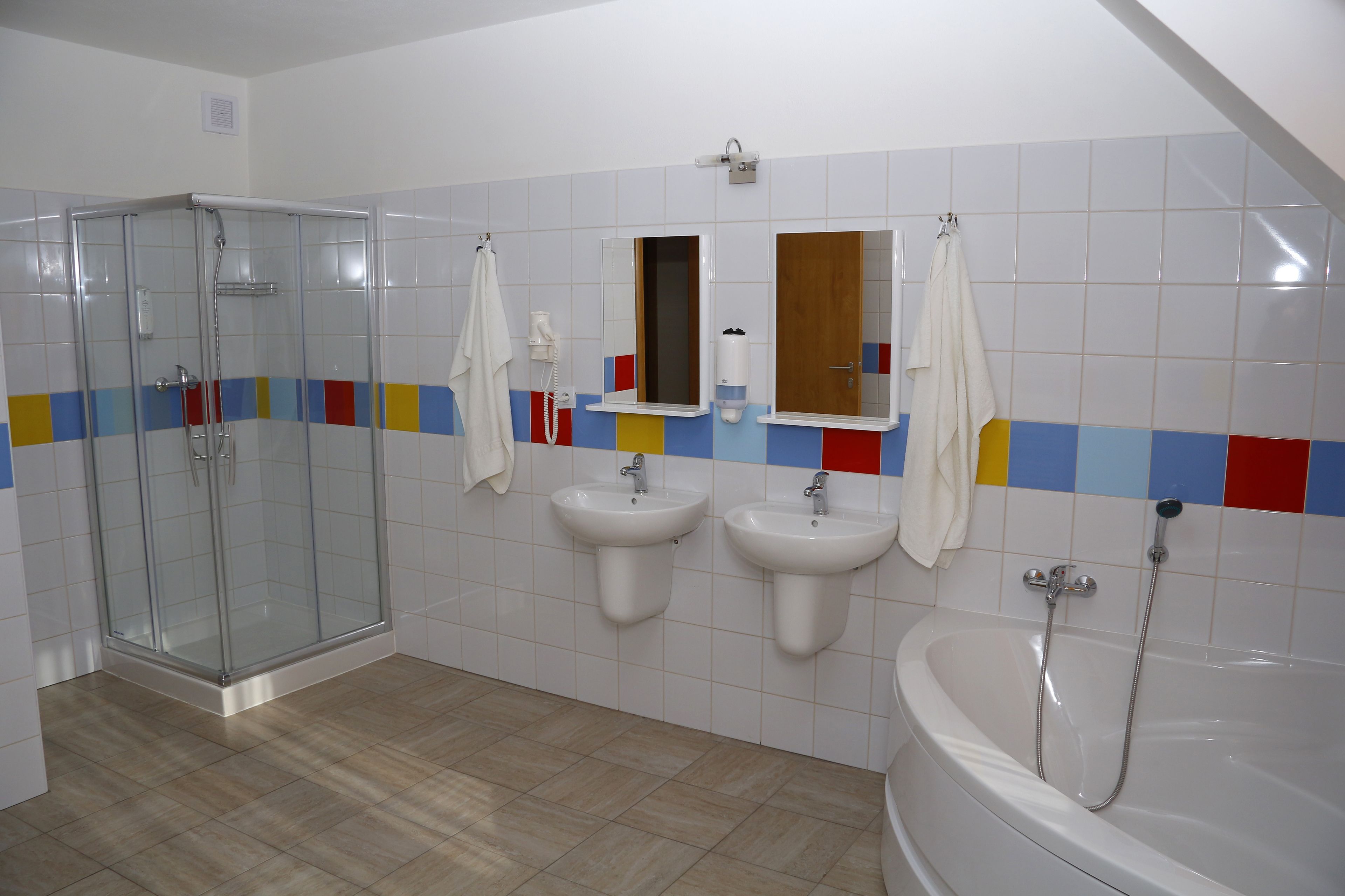 A bathroom with a glass-enclosed shower, two sinks, a bathtub, and colorful tiles on the wall.