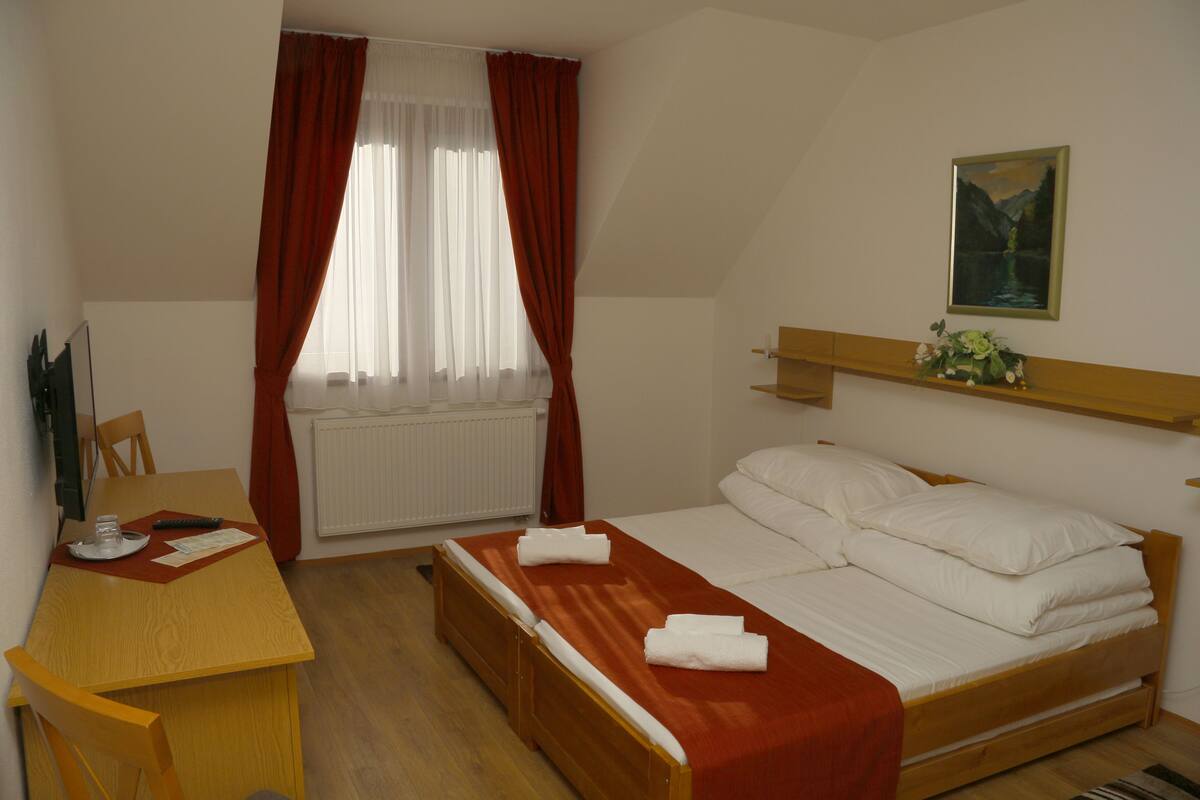 A bedroom with a bed, a wooden desk, a chair, a radiator, and a painting on the wall.