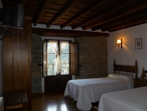 A room with two beds, wooden beams on the ceiling, a stone wall, and a window with curtains. - Casa Reda - Posada de Viñón (Cillorigo de Liebana)