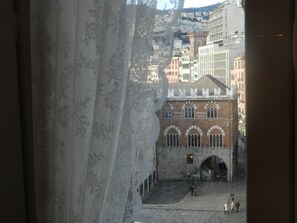 A view of a historic building with arched windows and a central archway, viewed through a window with a patterned curtain. - Bigo Guest House (Genoa)
