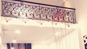 A modern bedroom with a bed, a hanging chair, a small table with plants, and a decorative railing. - Michi (Hanoi)