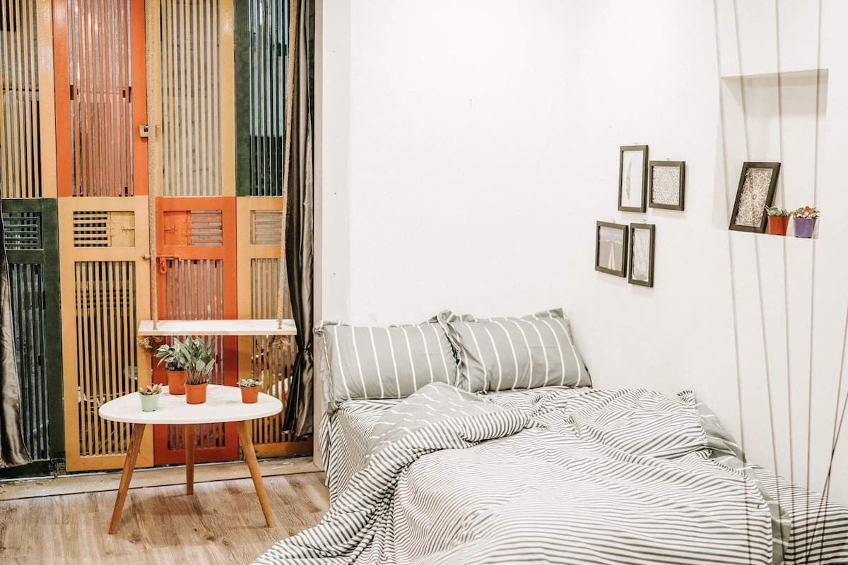 Una habitación con cama, una mesita con plantas y una pared decorada con cuadros.