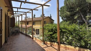 Un espacio al aire libre cubierto con piso de baldosas, pérgola de madera y una mesa con sillas.