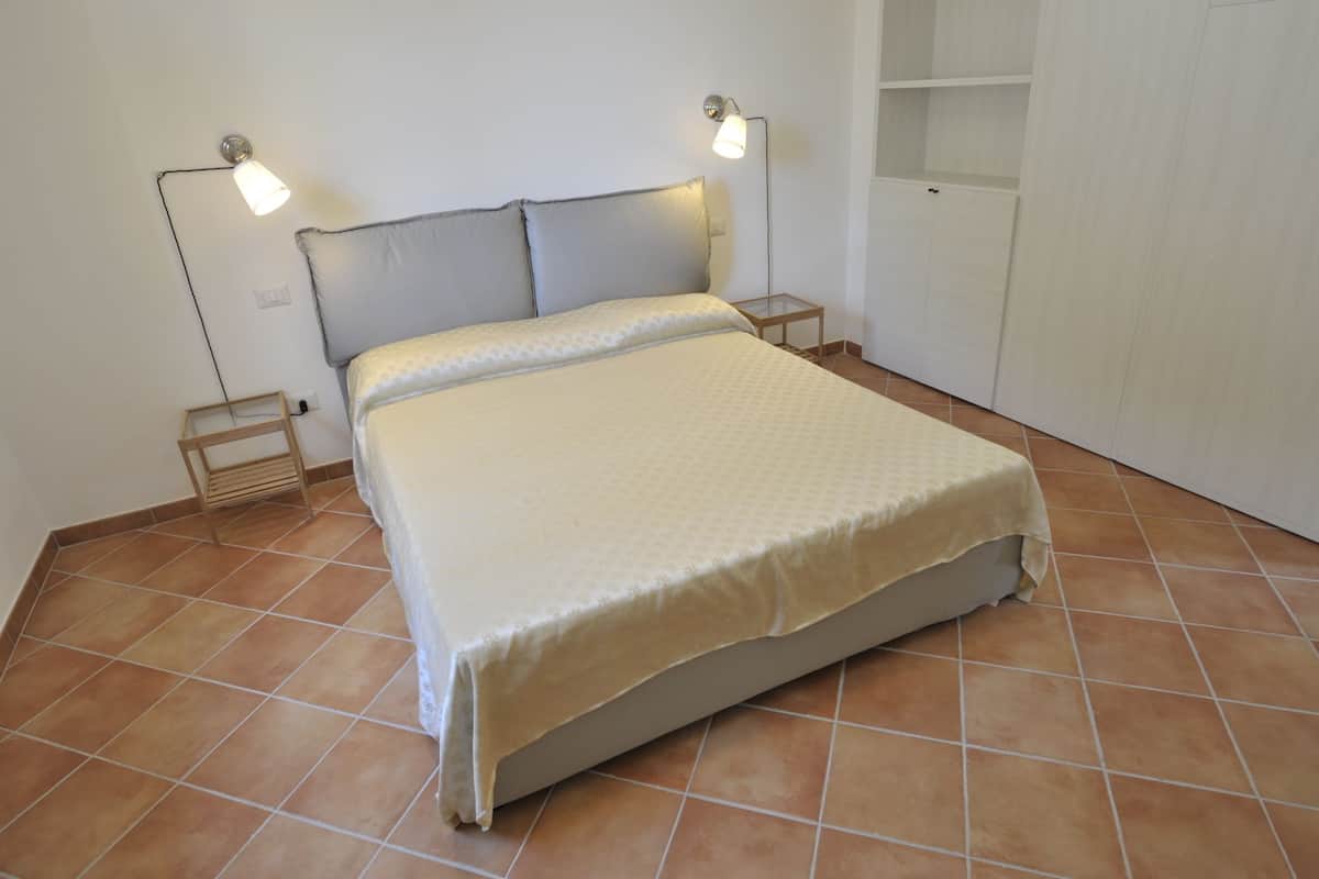 Habitación individual con piso de baldosas, dos mesitas de noche y un armario.