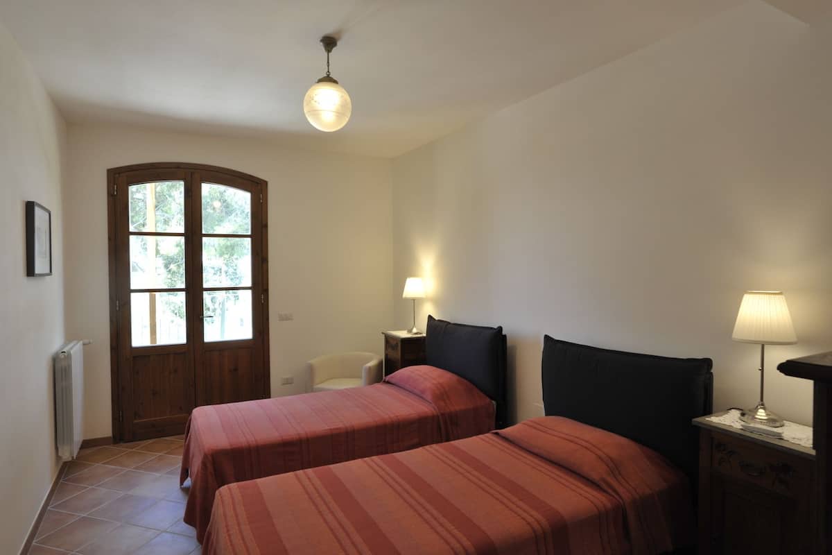 Una habitación con dos camas, una puerta de madera, un radiador, una silla y dos lámparas de noche.