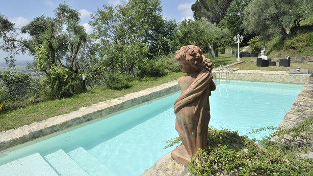 Una estatua junto a una piscina con vistas a árboles y un muro de piedra.