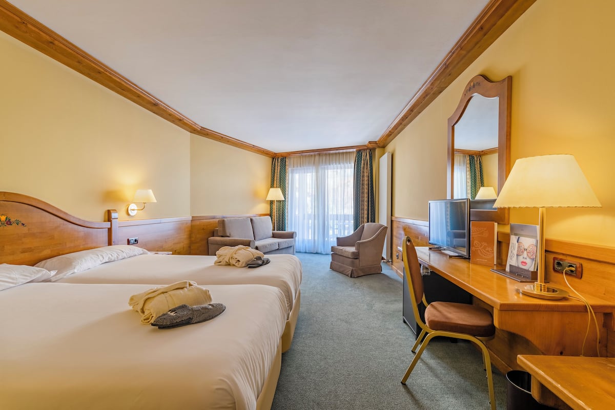 Habitación de hotel con dos camas, un escritorio con computadora, una silla y televisión.