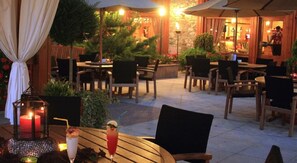 An outdoor dining area with tables and chairs, a Christmas tree, and a stone wall in the background. - Sport Village (Soldeu)