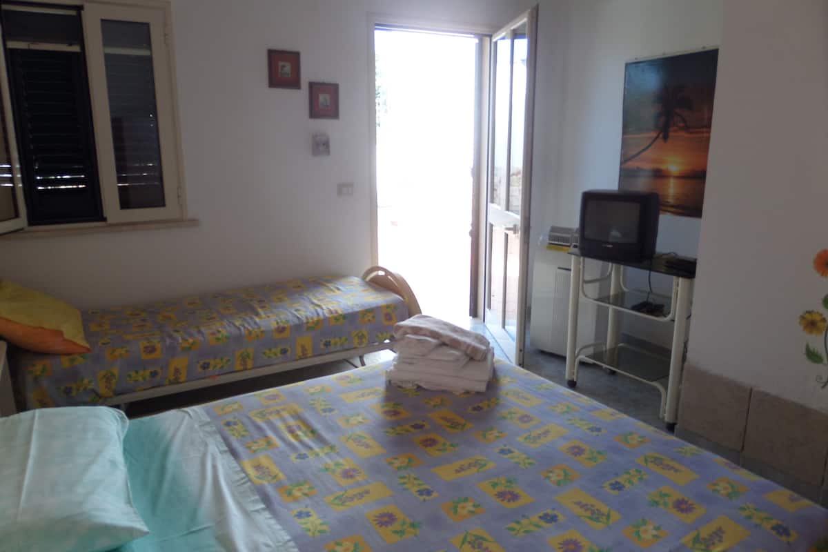 Habitación con dos camas, un televisor sobre un mueble y una puerta que da al exterior.
