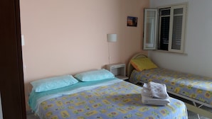 Une chambre avec deux lits simples, une table de chevet, une lampe et une fenêtre avec des stores.