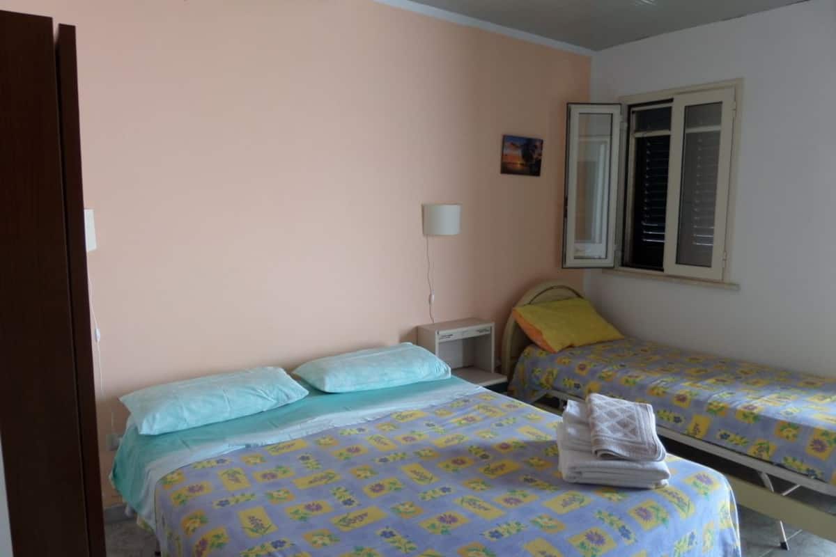 Un dormitorio con dos camas individuales, una mesita de noche, una lámpara y una ventana con persianas.