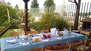 Un espace extérieur aménagé pour les repas, avec une table dressée pour quatre personnes, entourée de chaises, et un hamac en arrière-plan.