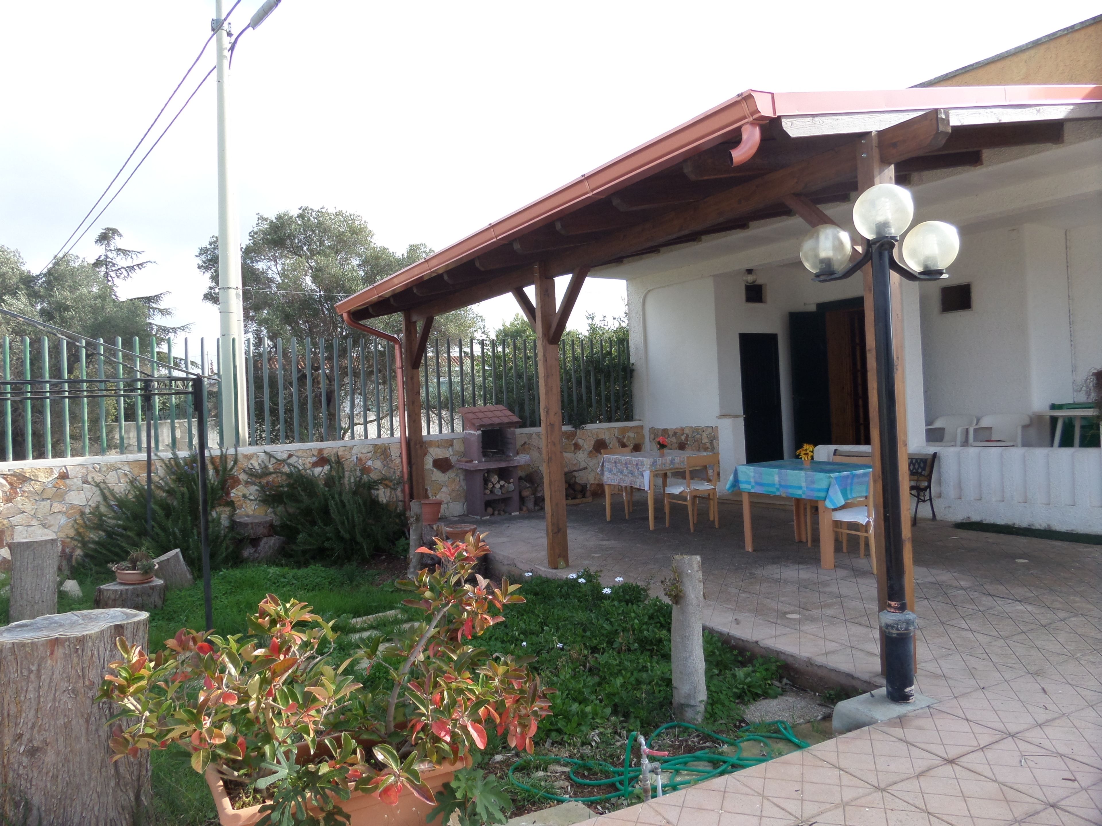 A covered outdoor patio with a table and chairs, a stone wall, and a wooden pergola.