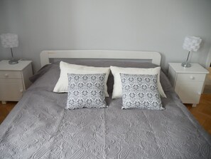 A neatly made bed with a patterned bedspread and two decorative pillows, flanked by white nightstands with lamps.