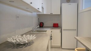 Cozinha compacta com armários brancos, geladeira, pia e bancada pequena com um objeto decorativo.