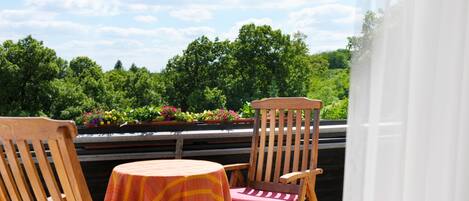 A balcony with two wooden chairs and a table, overlooking a garden with trees and flowers.