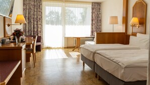 Ett hotellrum med två sängar, ett skrivbord med en lampa, en stol och utsikt över omgivningarna genom stora fönster.