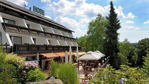 Ett hotell med en traditionell arkitektonisk stil, med en balkong prydd med blomlådor och en uteplats med utomhusmöbler.