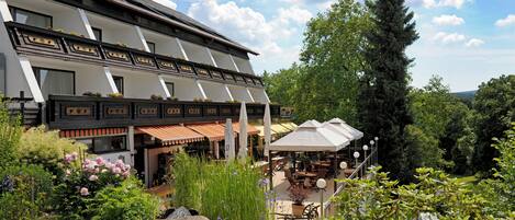 A hotel with a traditional architectural style, featuring a balcony with flower boxes and a patio area with outdoor seating.